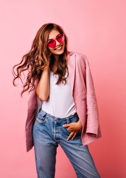 Excited white girl in bright stylish glasses posing on pink. Dreamy curly woman playing with her ginger hair and laughing.